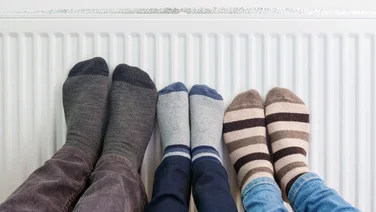 Three people put their feet on a radiator powered through a boiler