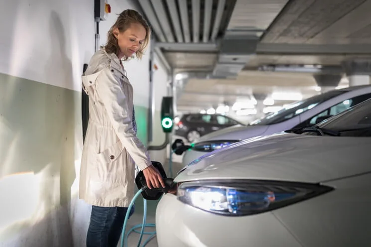 Young woman charging an electric vehicle in an underground garage equiped with e-car charger