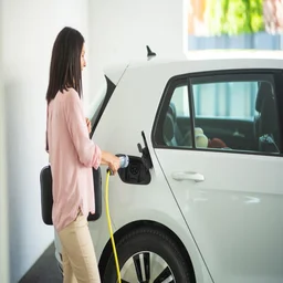 woman plugging in a charger to an electric vehicle in a garage