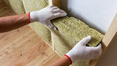 Person wearing white gloves slotting insulation blocks of fibreglass into a wall