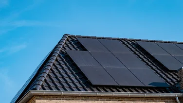 black solar panels on a dark roof under a blue sky