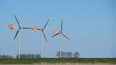 three small wind turbines in a field with trees in distance