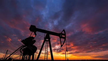A silhouette of a fracking machine working in a sandy environment at sunset