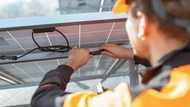 Installer in an orange hard hat and high vis jacket handling wires at the back of a solar panel