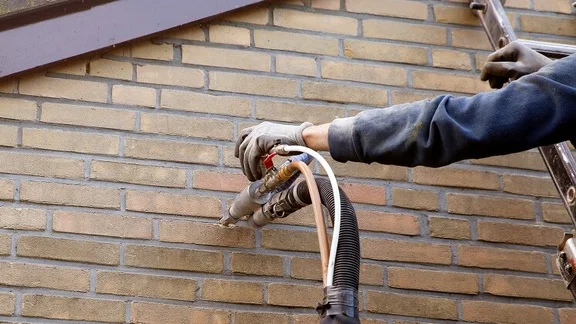 Someone Installing cavity wall insulation into the wall through a small hole
