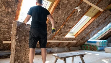 Someone stood in a light loft with windows installing roof insulation panels