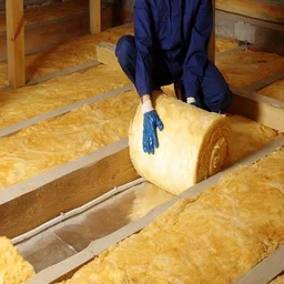 An installer dressed in navy overalls rolls out yellow fibre floor insulation