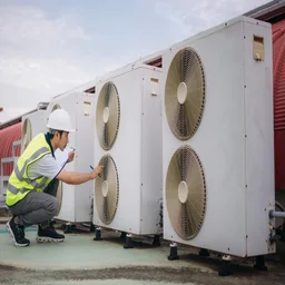 an engineer in a fluorescent jacket checking on heat pumps on a roof