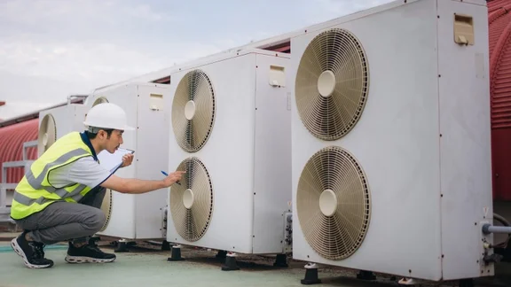 an engineer in a fluorescent jacket checking on heat pumps on a roof