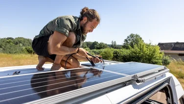 man on the roof of a camper van, connecting black solar panels
