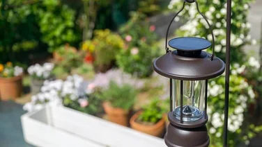 solar-powered lantern hanging from metal pergola in flowery garden