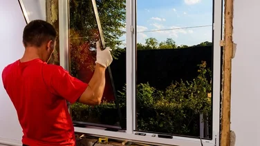 Someone in a red shirt holding a panel of glass whilst installing double glazed windows
