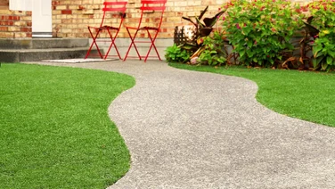 Garden with two red chairs and a grey wiggly pathway bordered by green artificial grass