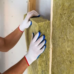 Installer with white and blue gloves on puts a panel of rock wool insulation into the wall