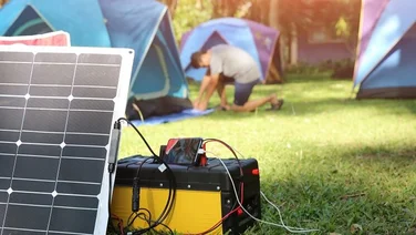 portable solar generator connected to solar panels with man setting up tents in background