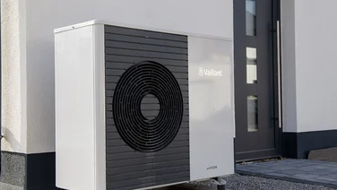 air source heat pump outside house with gravel entrance and white walls