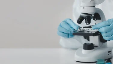 scientist wearing rubber gloves and lab coat looking through microscope