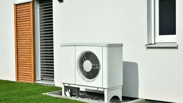 white heat pump unit outside home with green lawn and white walls