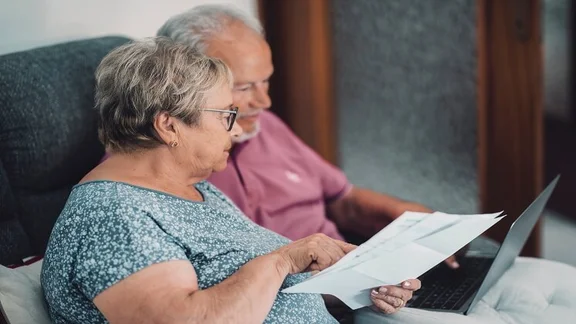 Side view of elderly couple at home paying bills online via laptop