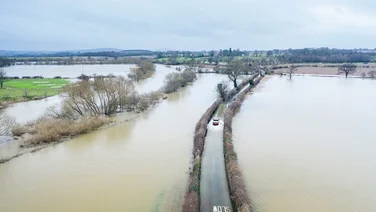 car driving on road with flooded fields on either side