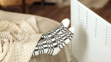 woman's feet in socks warming near electric heater