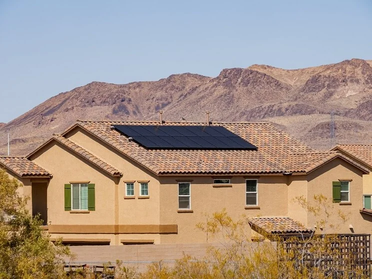 View of a two-story house with solar panels on roof and desert mountains in the background