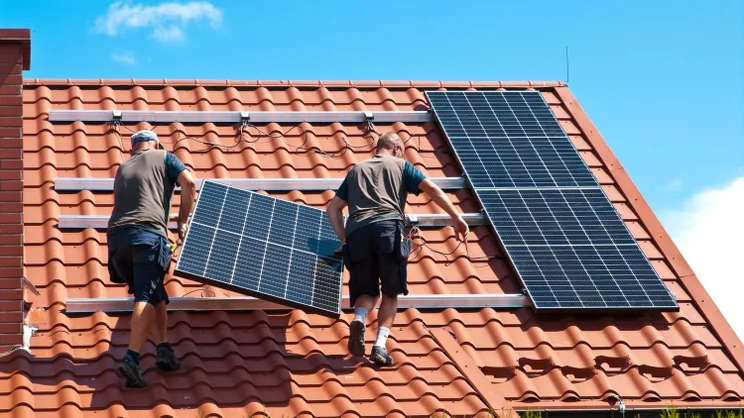 Dva muži nesoucí solární panel na střechu